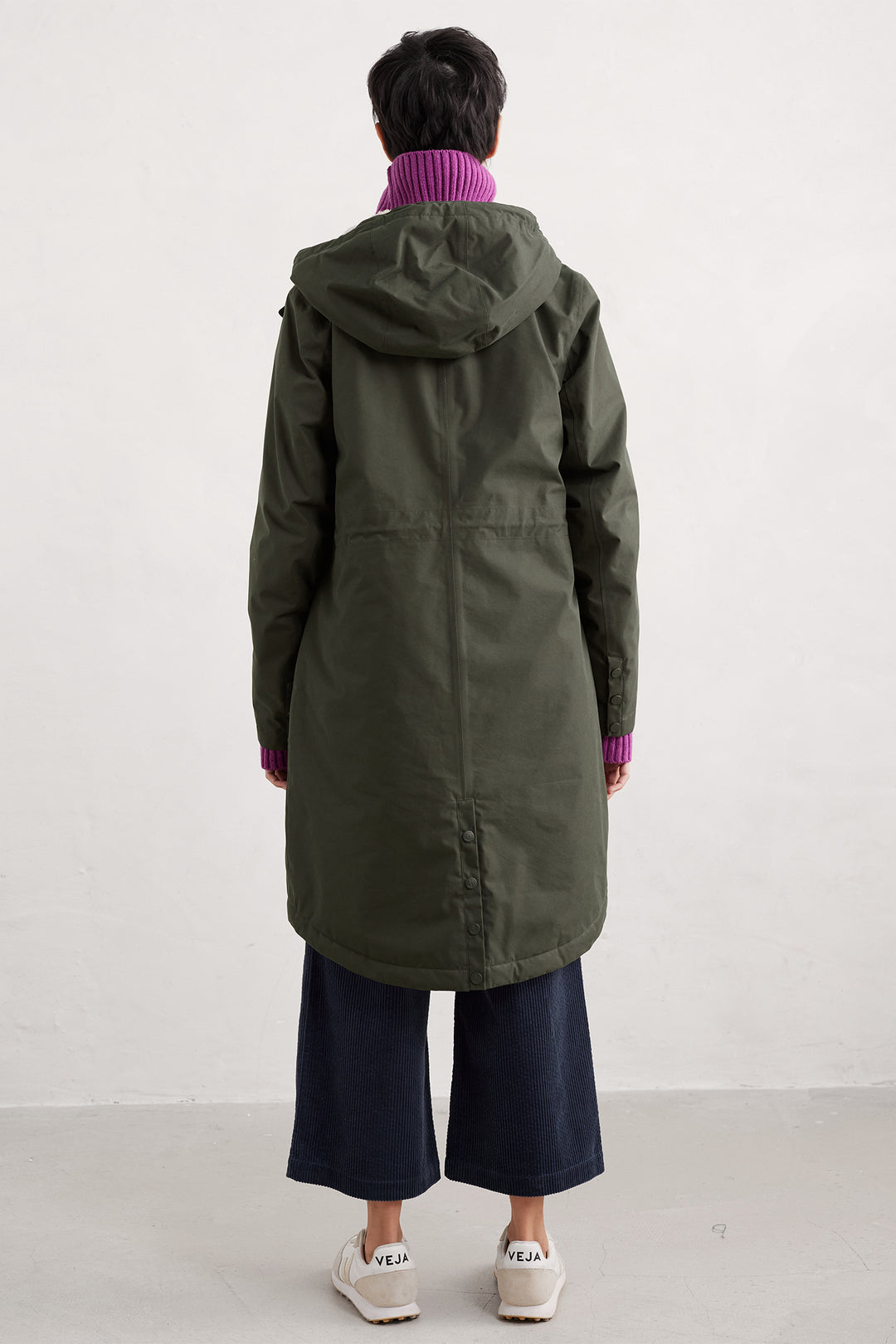 Person wearing a long green coat with a hood on a white background