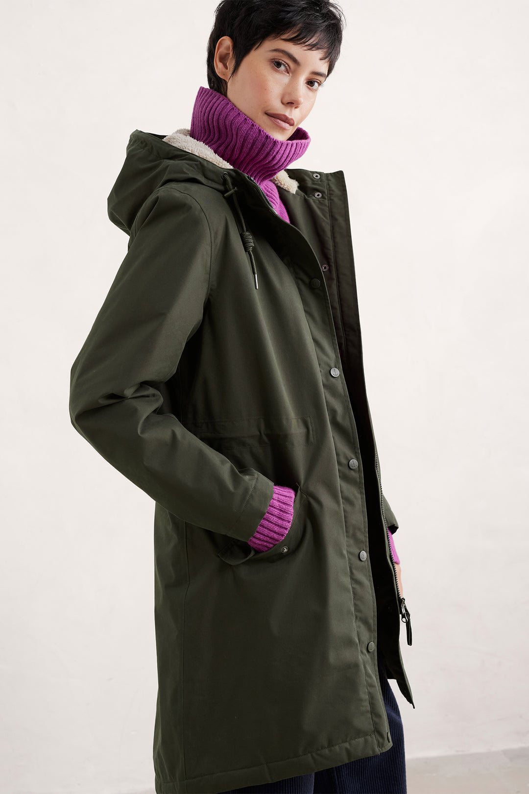 Person wearing a green coat with a purple scarf against a white background