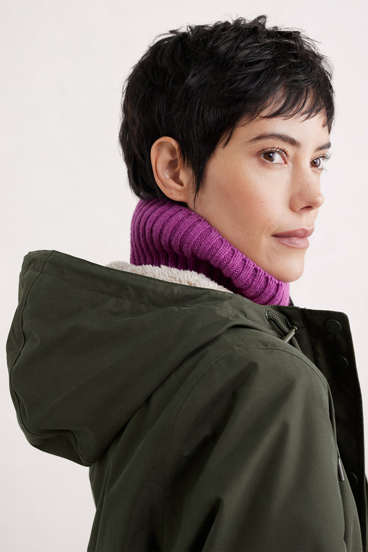 Person wearing a green hooded coat with a purple knitted sweater underneath on a white background