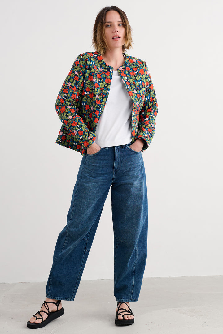 Woman wearing a colorful floral jacket, white shirt, blue jeans, and black sandals on a white background