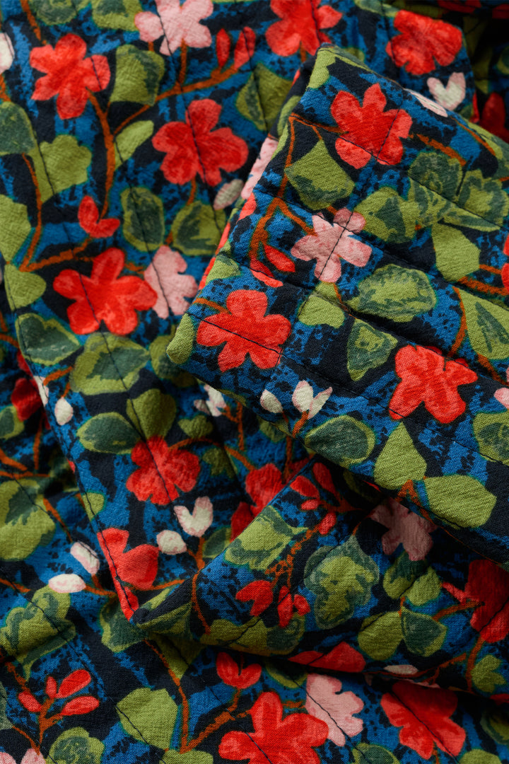 Close-up of a floral patterned fabric with red, pink, and green flowers on a dark blue background.