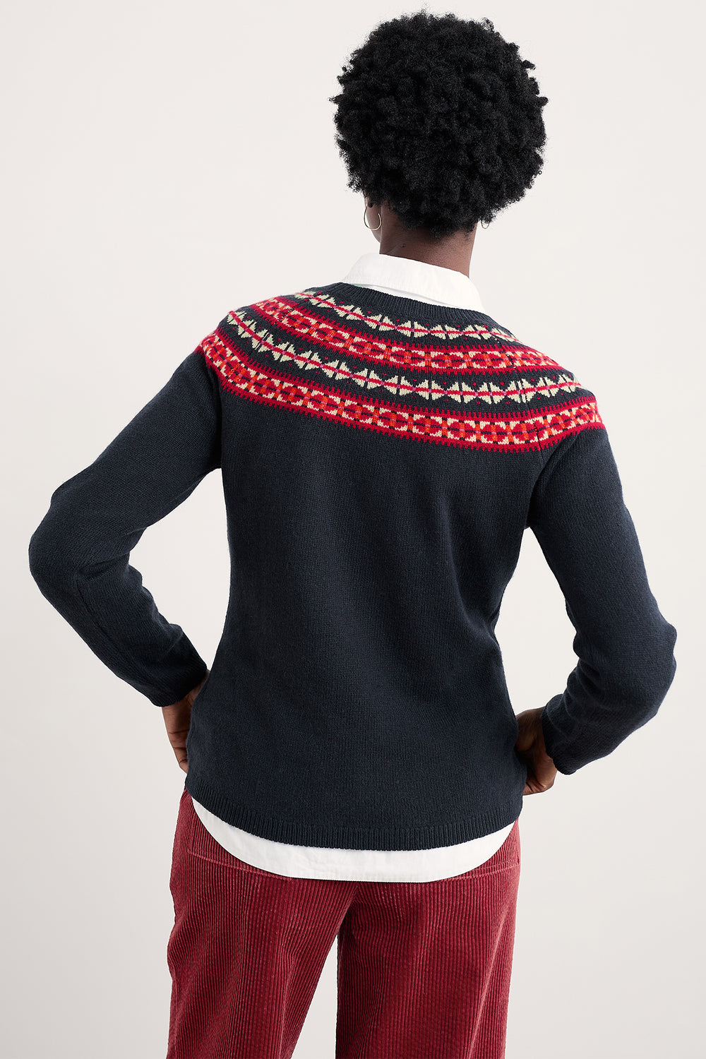 Person wearing a navy sweater with a red and white pattern on a plain background