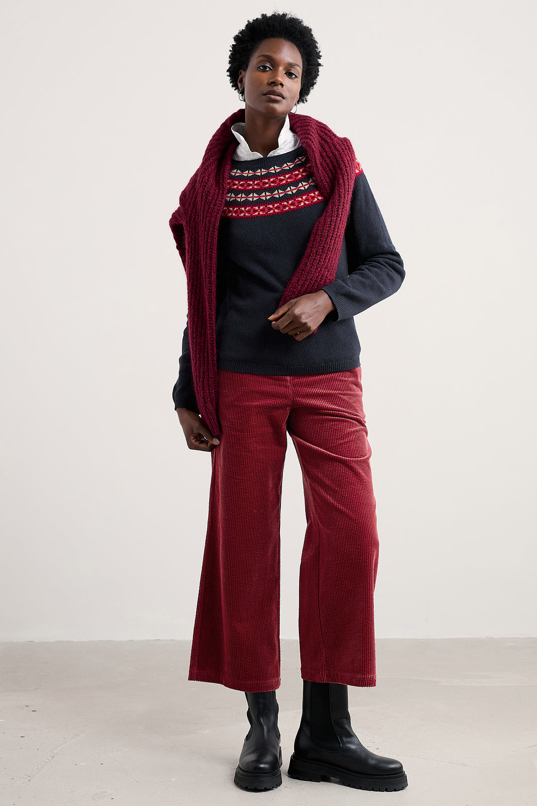 Person wearing a dark sweater, red scarf, and red pants on a white background