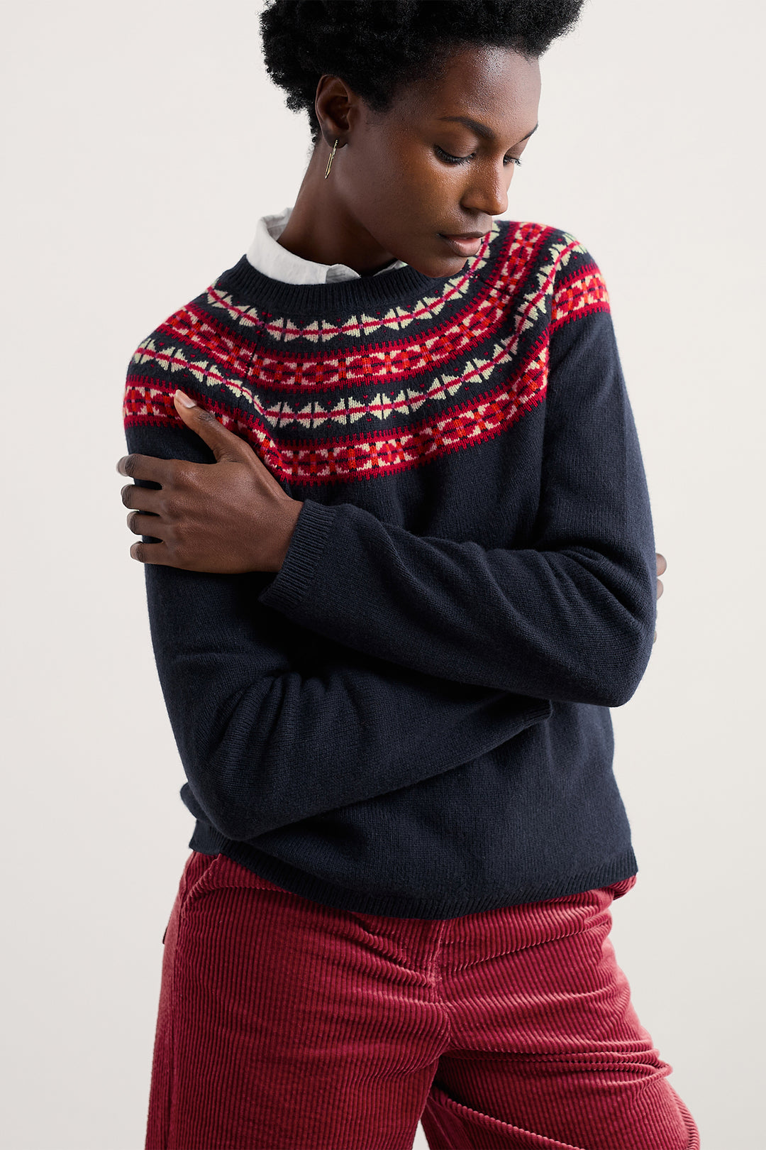 Person wearing a dark blue sweater with a red and white patterned collar against a plain background