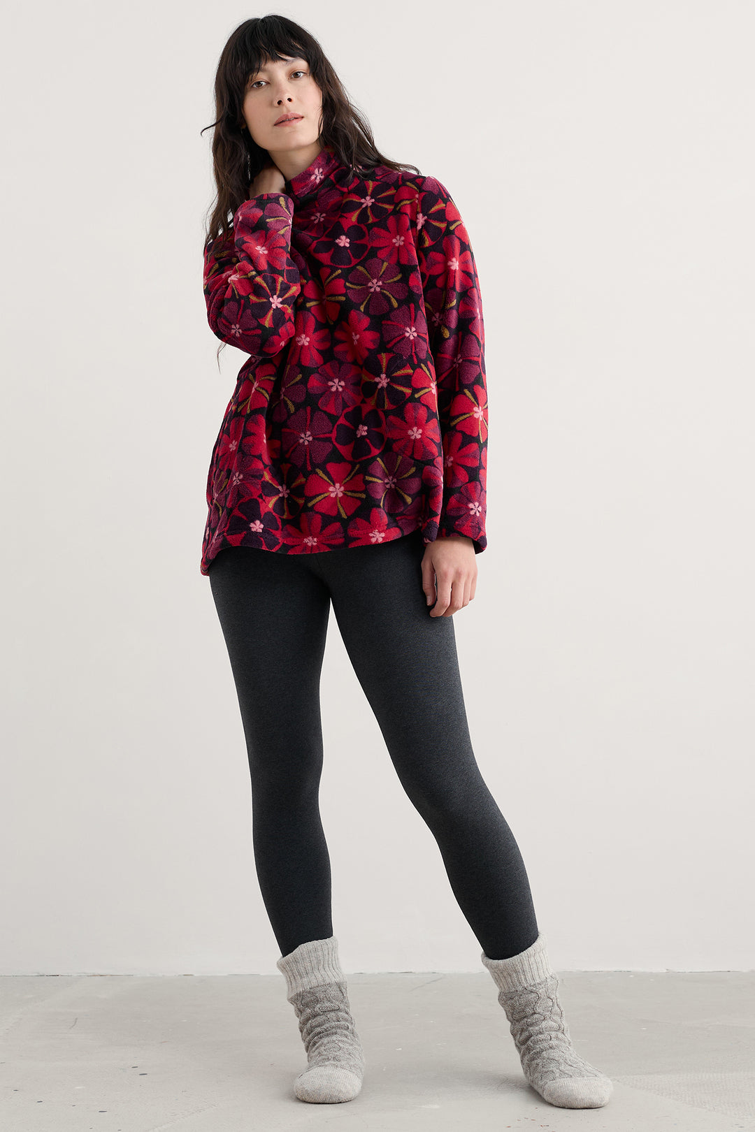Person wearing a red patterned jacket, black leggings, and gray socks on a white background