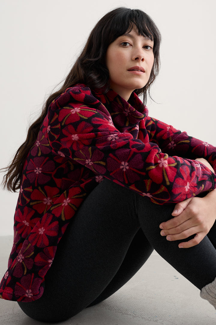 Woman wearing a red floral jacket sitting on a white floor.