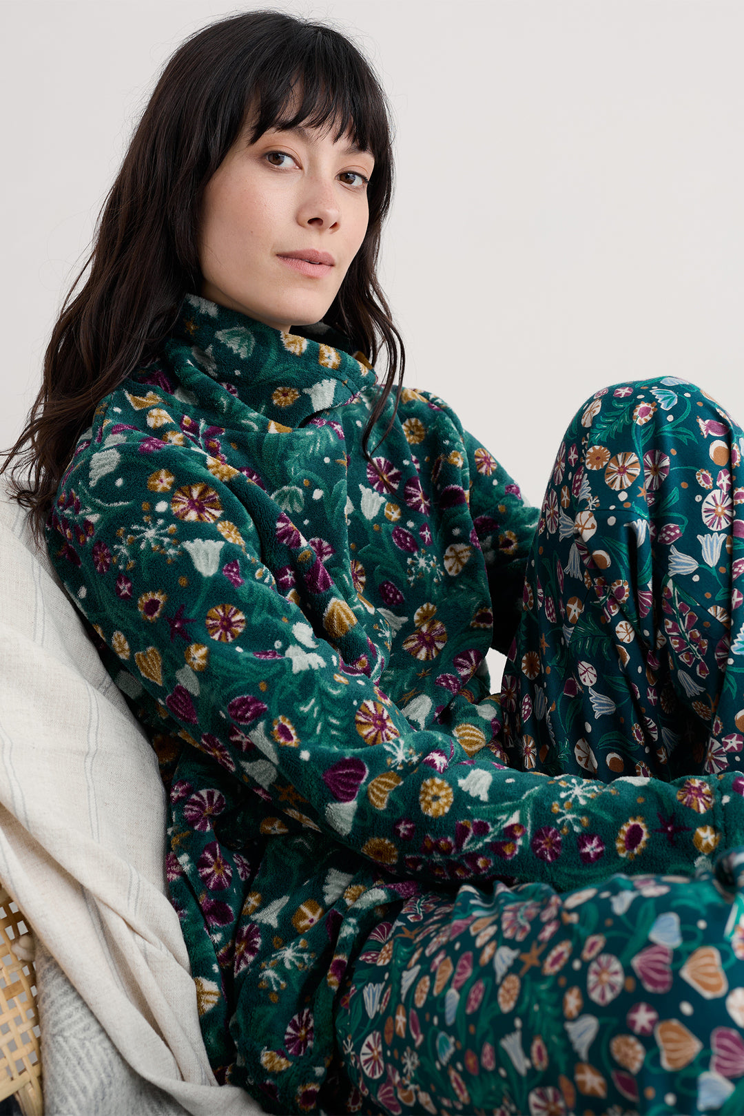Woman wearing a dark green floral patterned outfit sitting on a white surface.