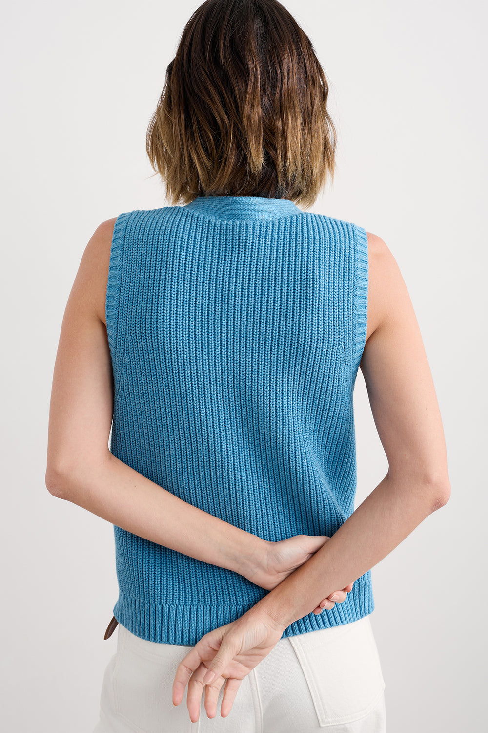 Person wearing a blue sleeveless knitted top against a white background