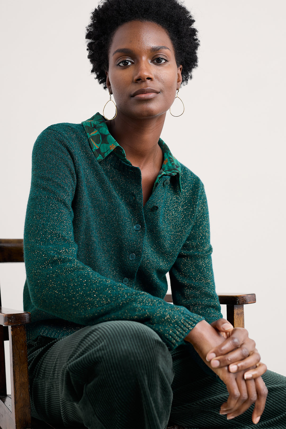 Woman wearing a green knitted sweater sitting on a wooden chair.