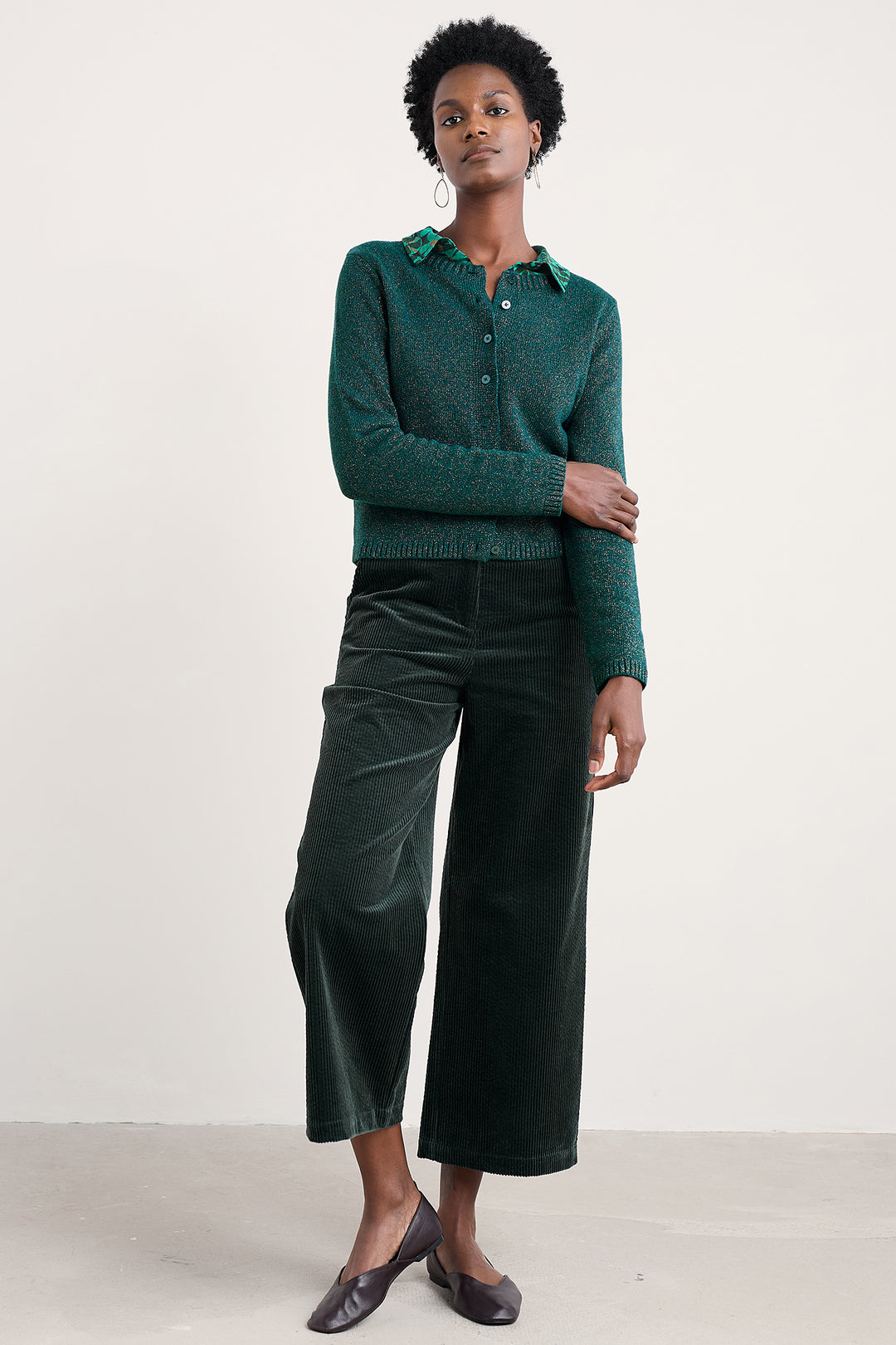 Woman wearing a green knitted cardigan and dark green pants against a white background