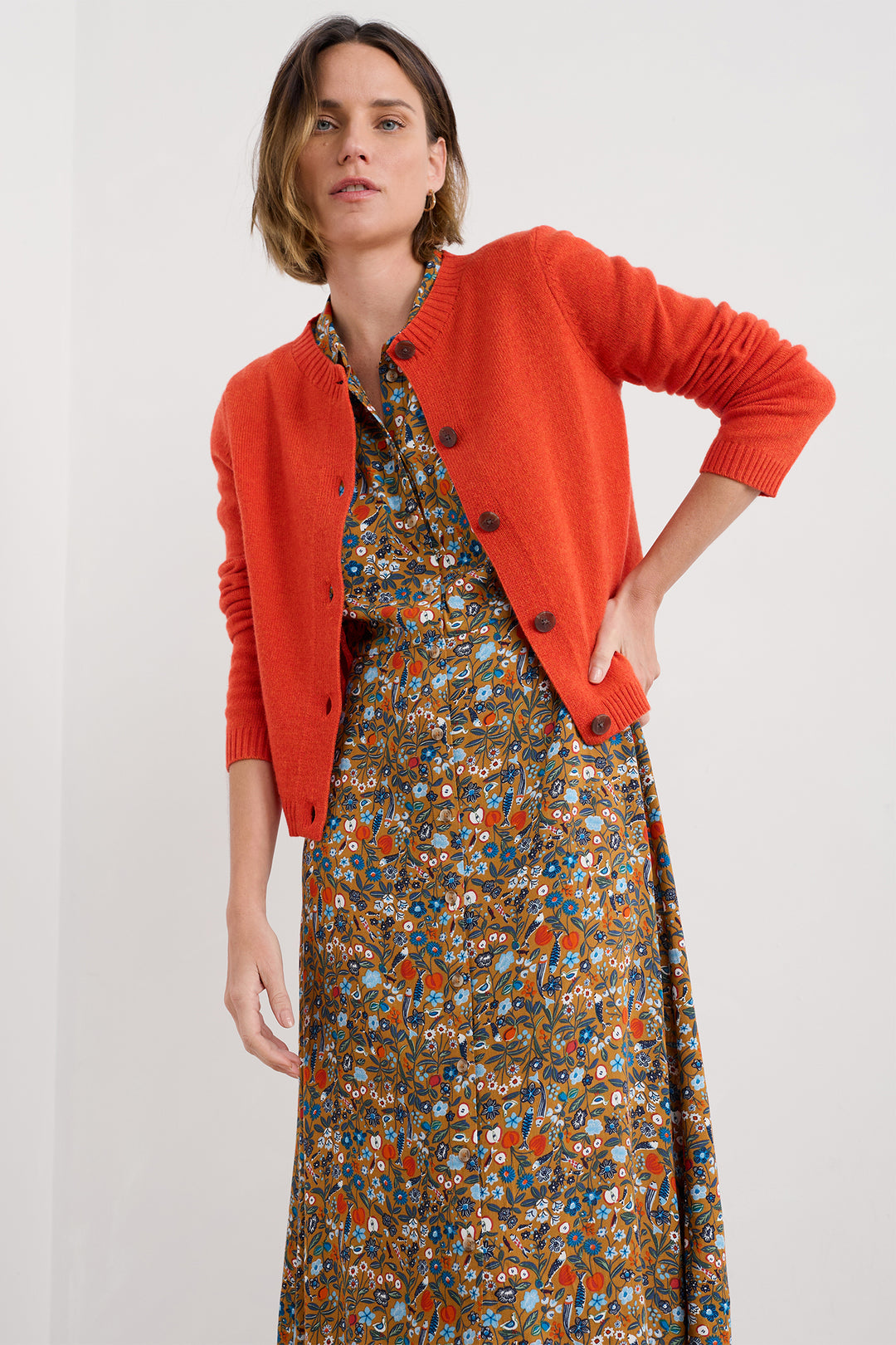 Woman wearing a floral dress and orange cardigan on a white background