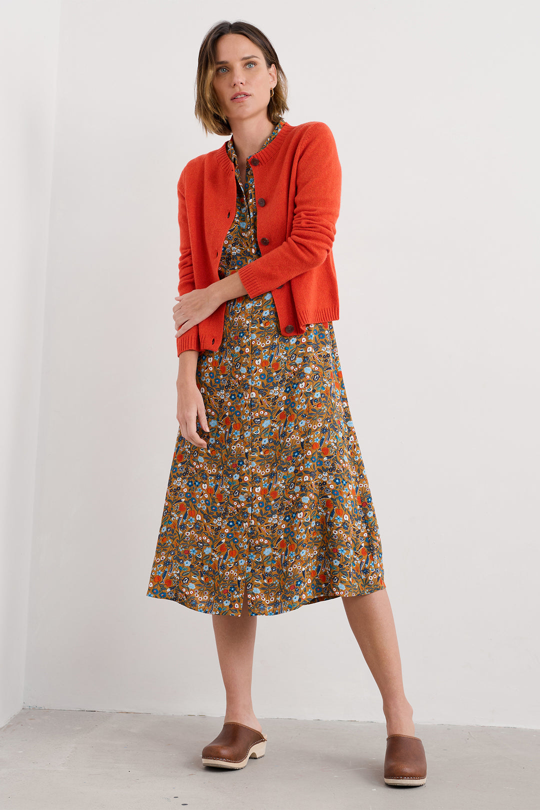 Woman wearing a orange cardigan and floral dress on a white background