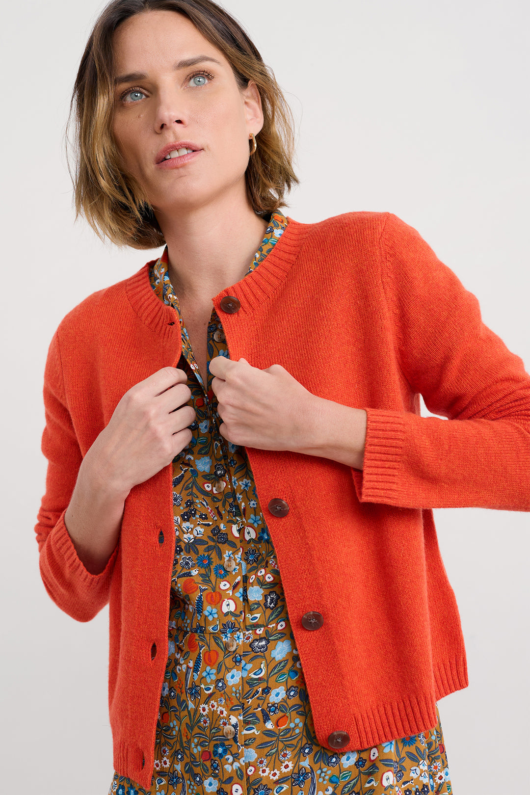 Woman wearing an orange cardigan over a patterned dress on a white background