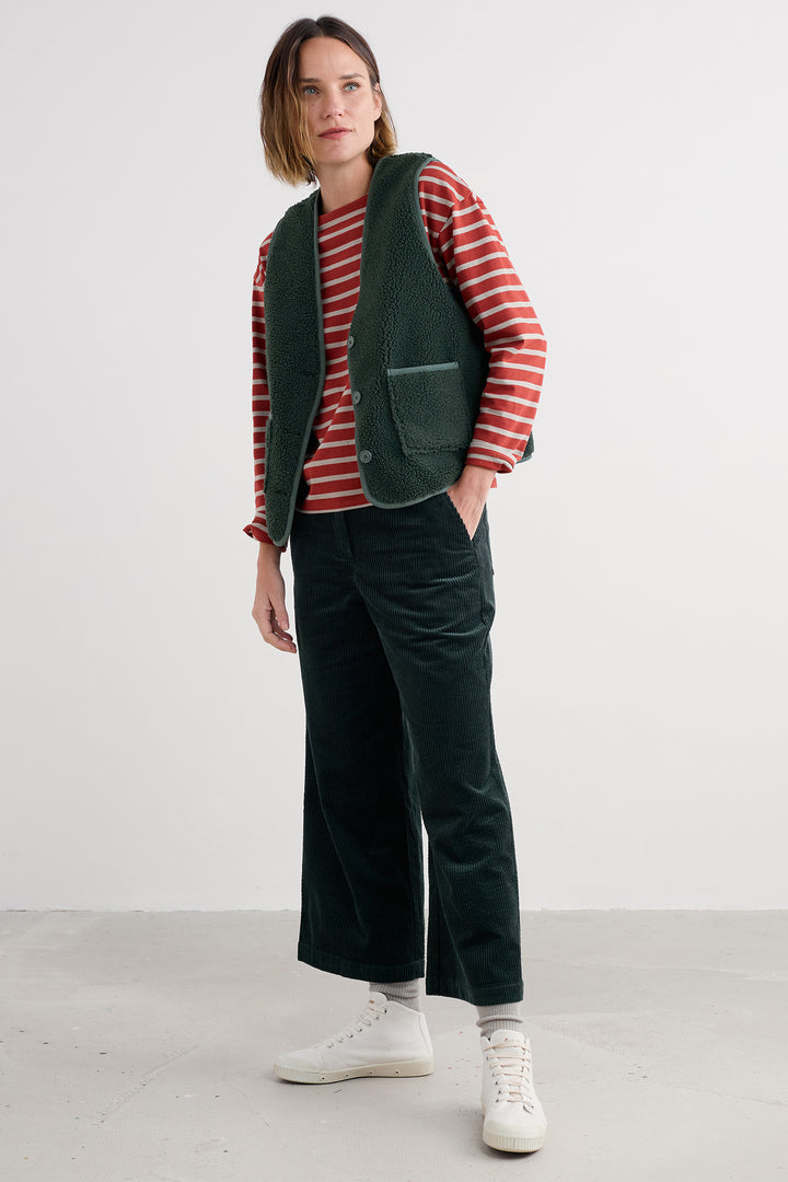 Woman wearing a red and white striped shirt, green vest, and dark green pants on a white background