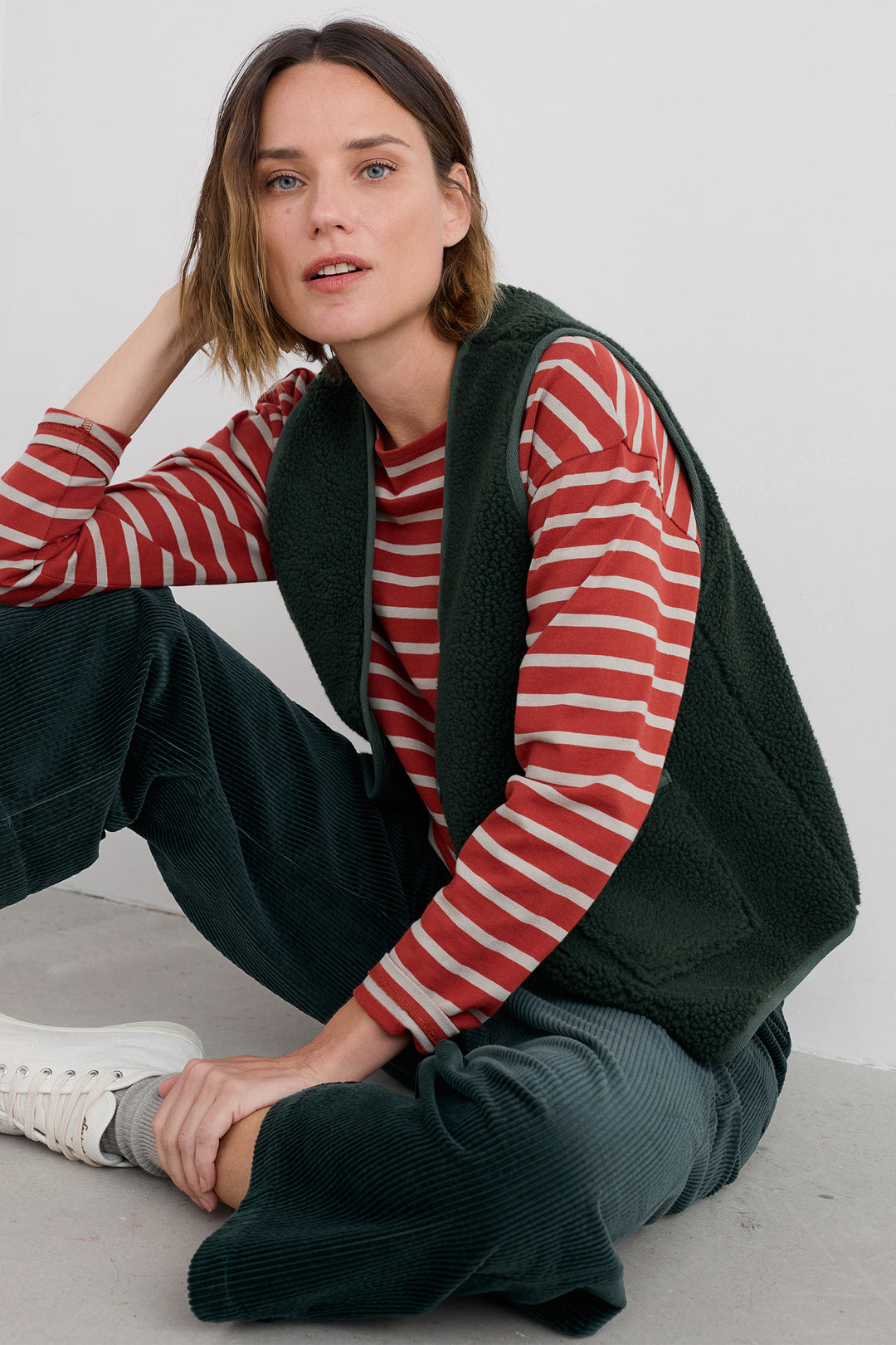 Woman wearing a red and white striped shirt with a green vest sitting on a gray surface.