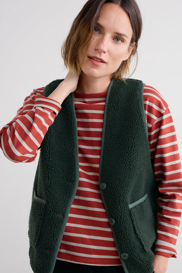 Woman wearing a green fleece vest over a red and white striped shirt on a plain background