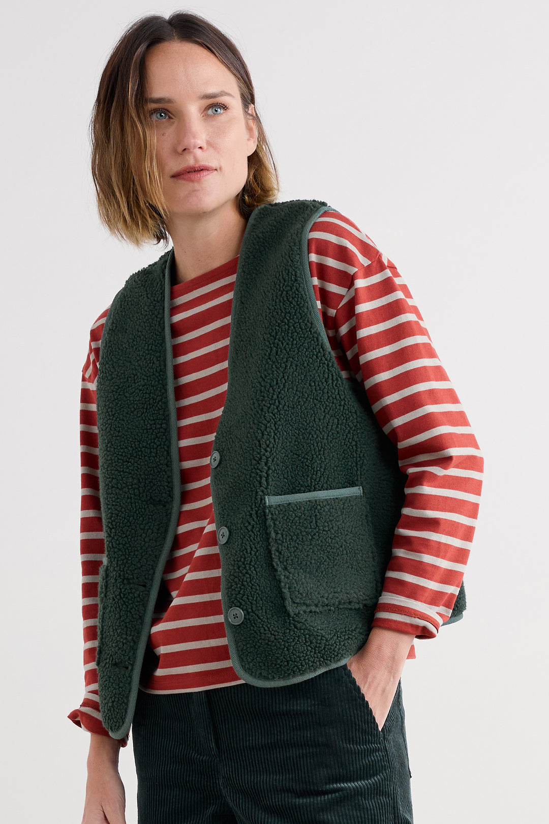 Person wearing a green vest over a red and white striped shirt on a white background