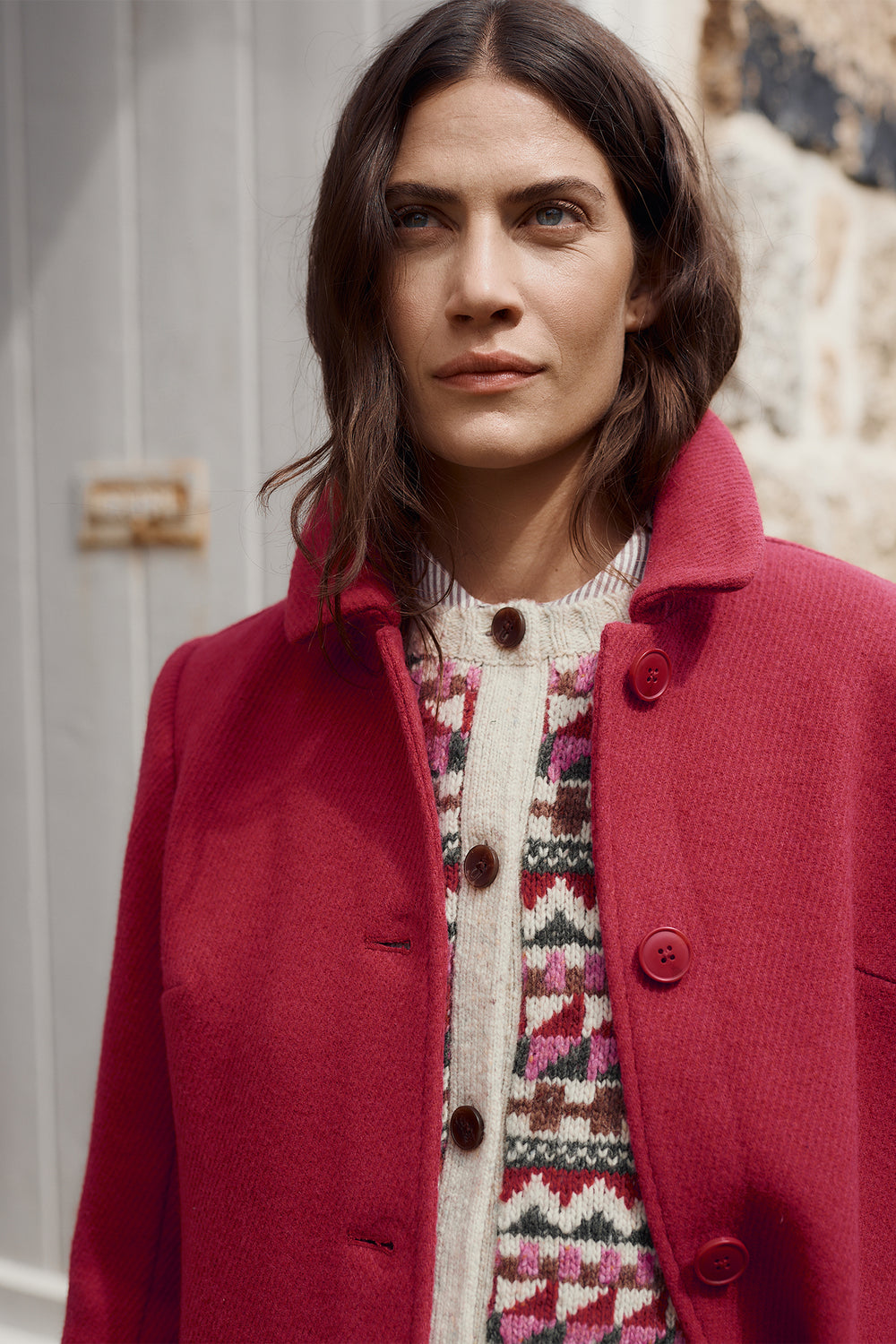 Woman wearing a red coat over a patterned sweater against a neutral background