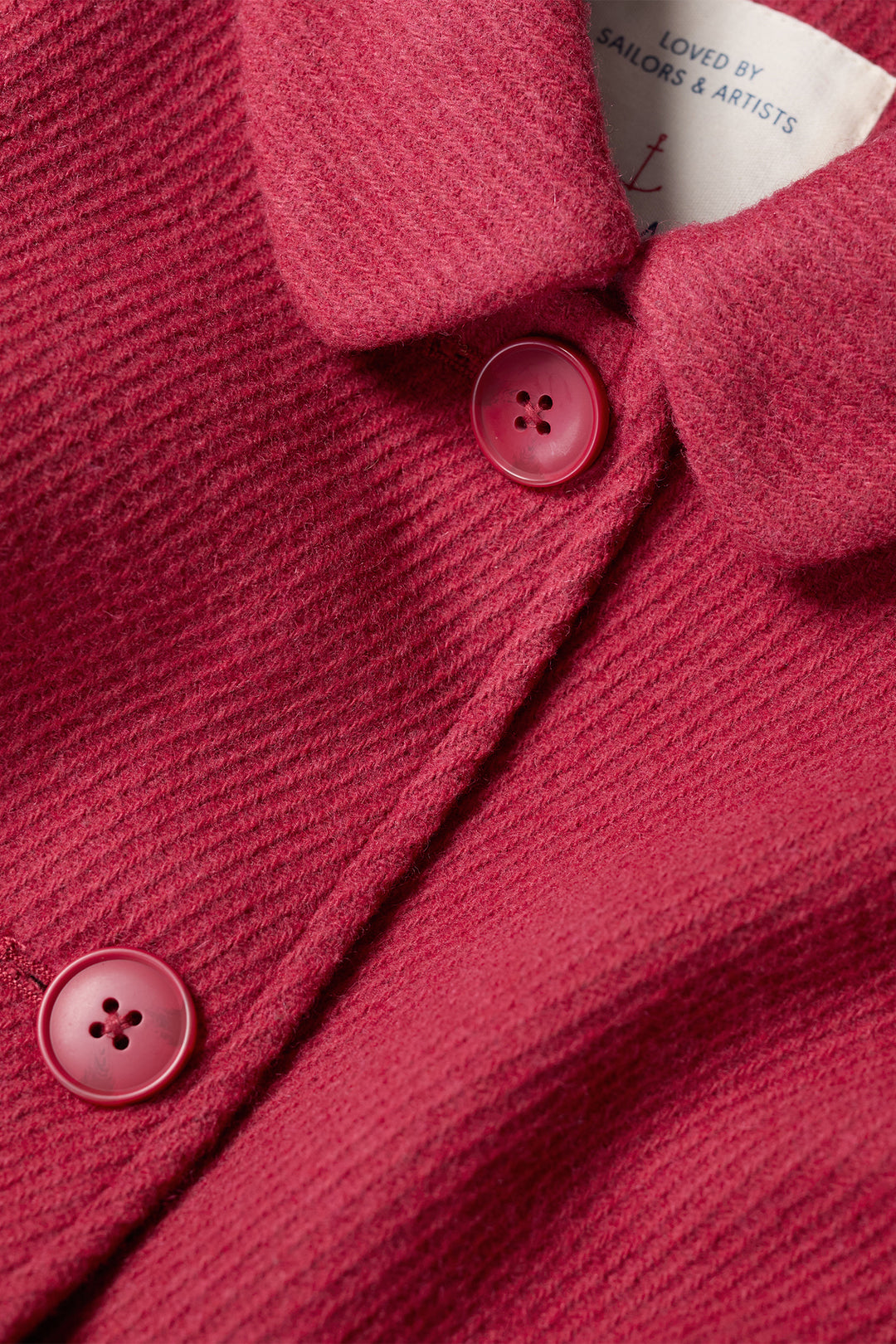 Close-up of a red textured garment with buttons and a brand label.