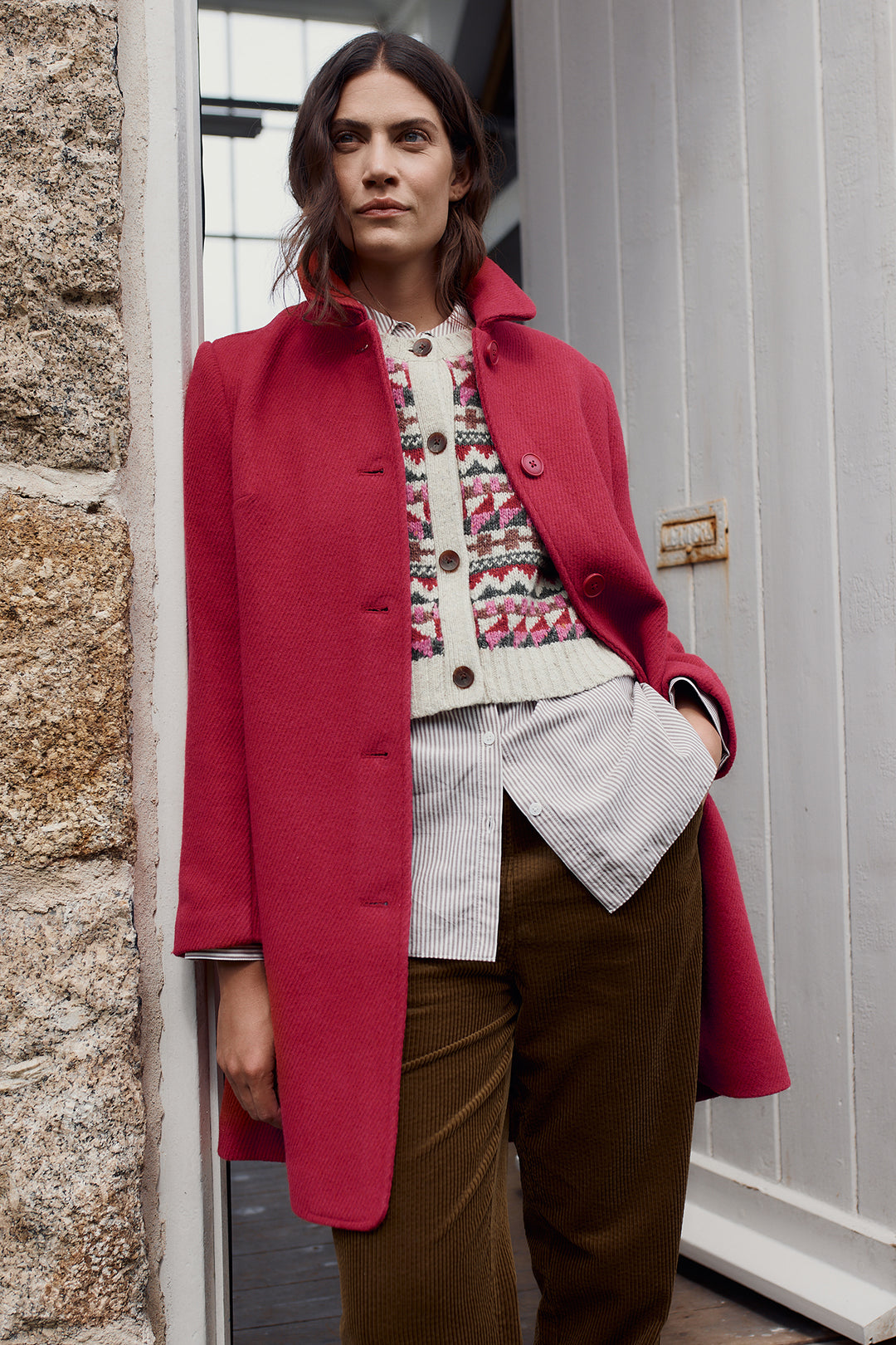 Woman wearing a red coat standing against a stone wall.