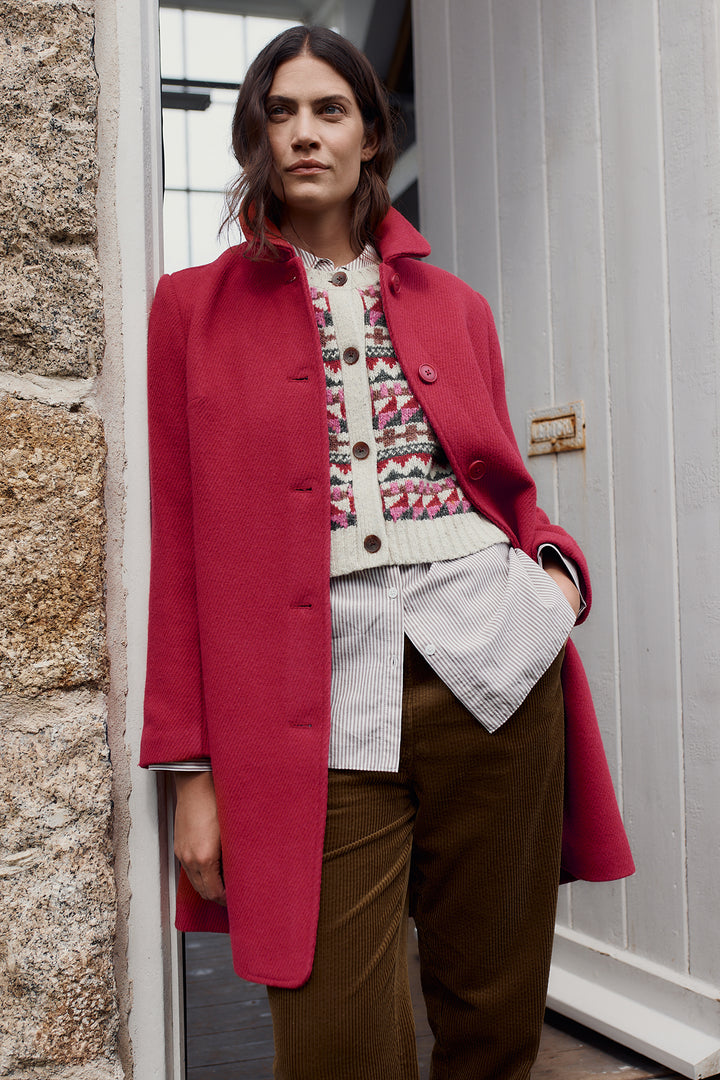 Woman wearing a red coat standing against a stone wall.