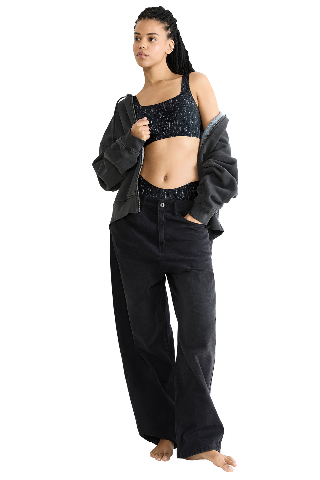 Woman wearing a black sports bra and pants with a gray jacket on a white background