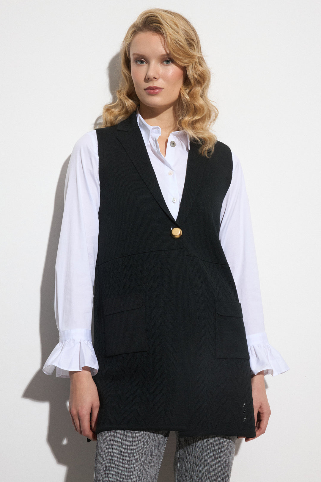 Woman wearing a black vest over a white shirt with a plain background