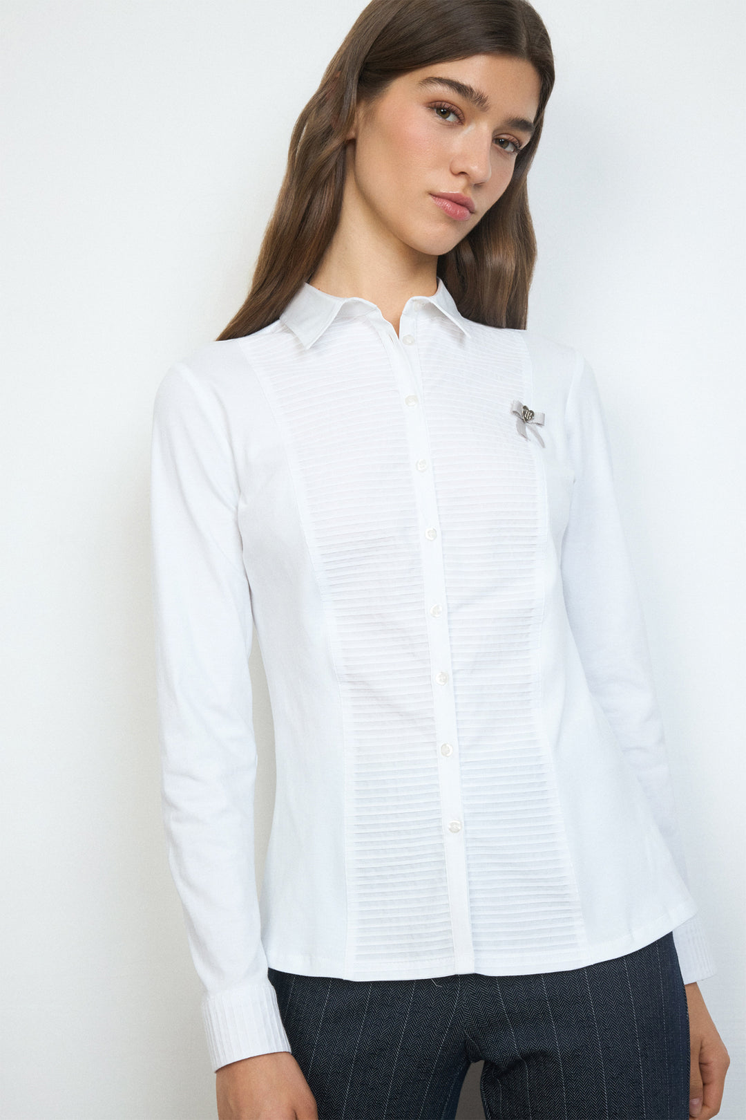 Woman wearing a white button-up shirt with a small logo on a plain background
