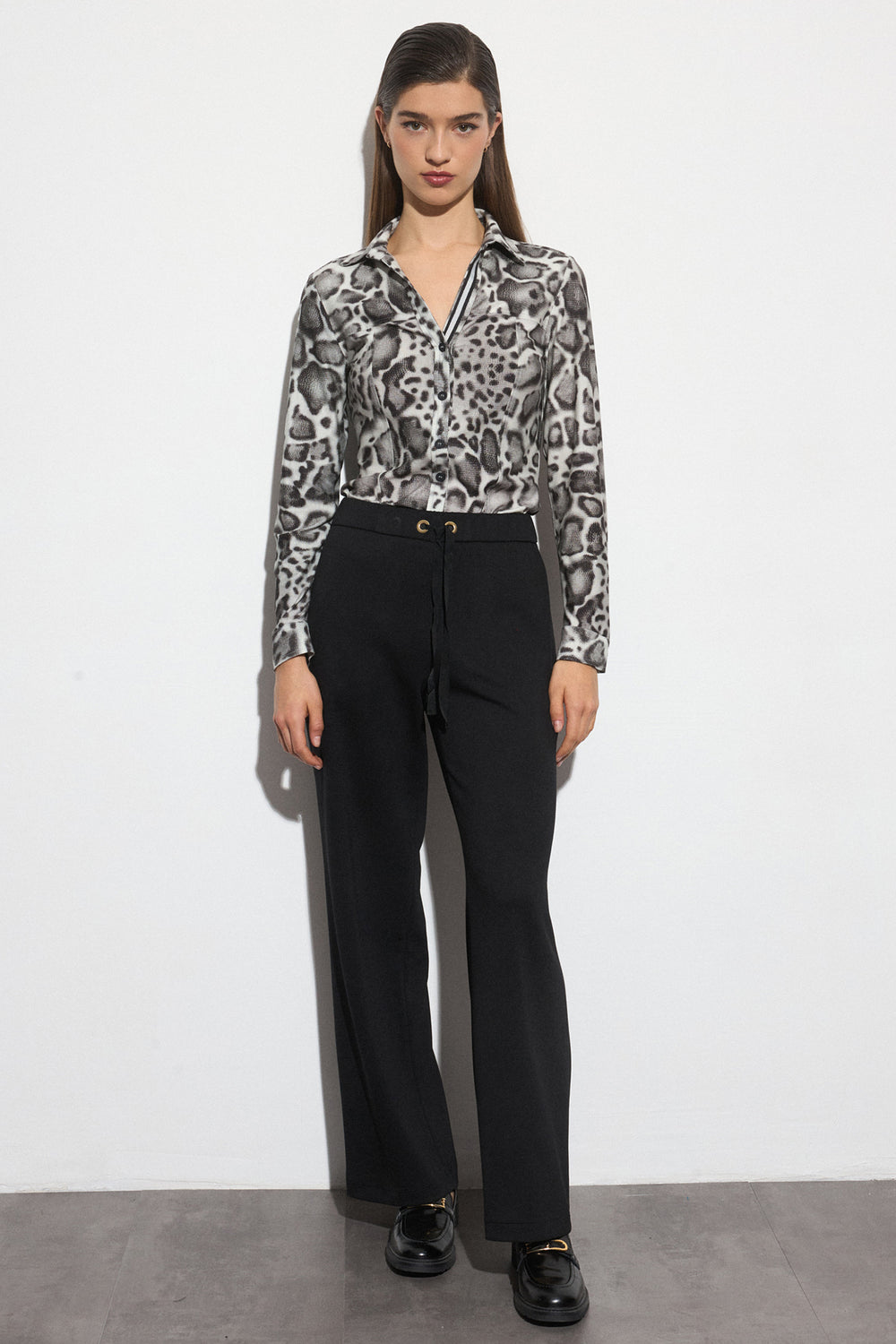 Woman wearing a patterned blouse and black pants against a white background
