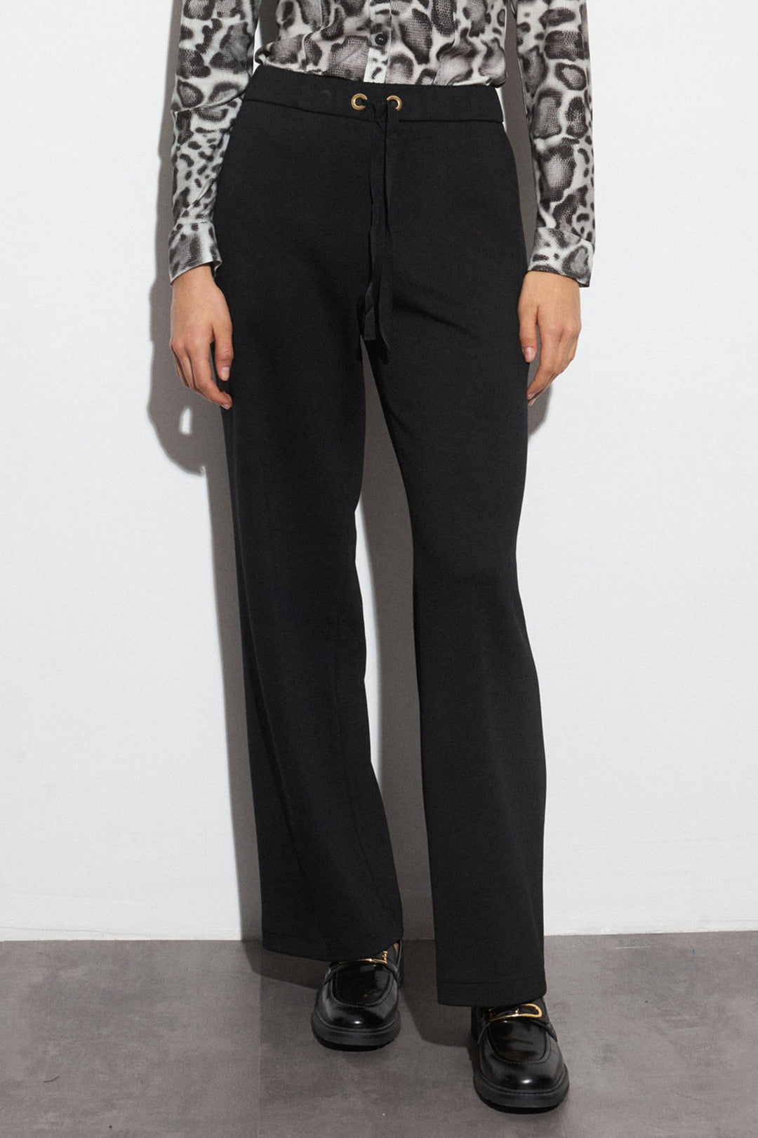 Person wearing black pants with a patterned top against a white background