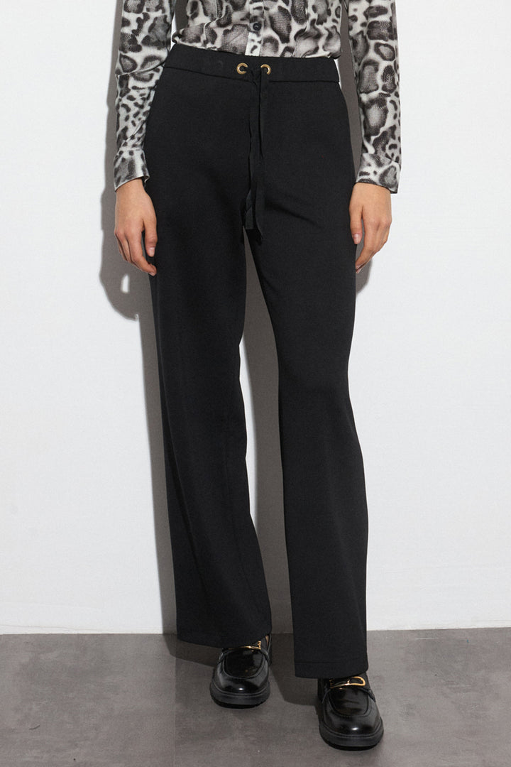 Person wearing black pants with a patterned top against a white background