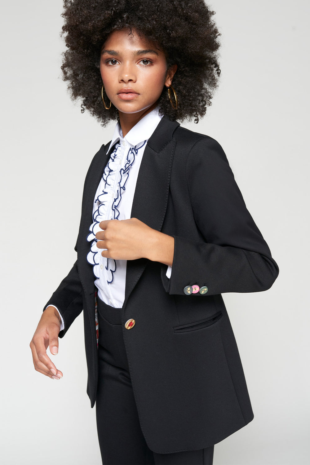 Woman wearing a black blazer over a white shirt with blue patterns on a plain background