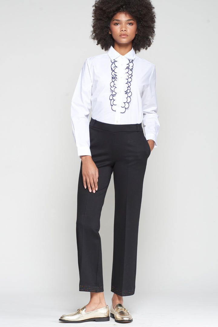 Person wearing a white blouse with black embroidery and black pants on a white background