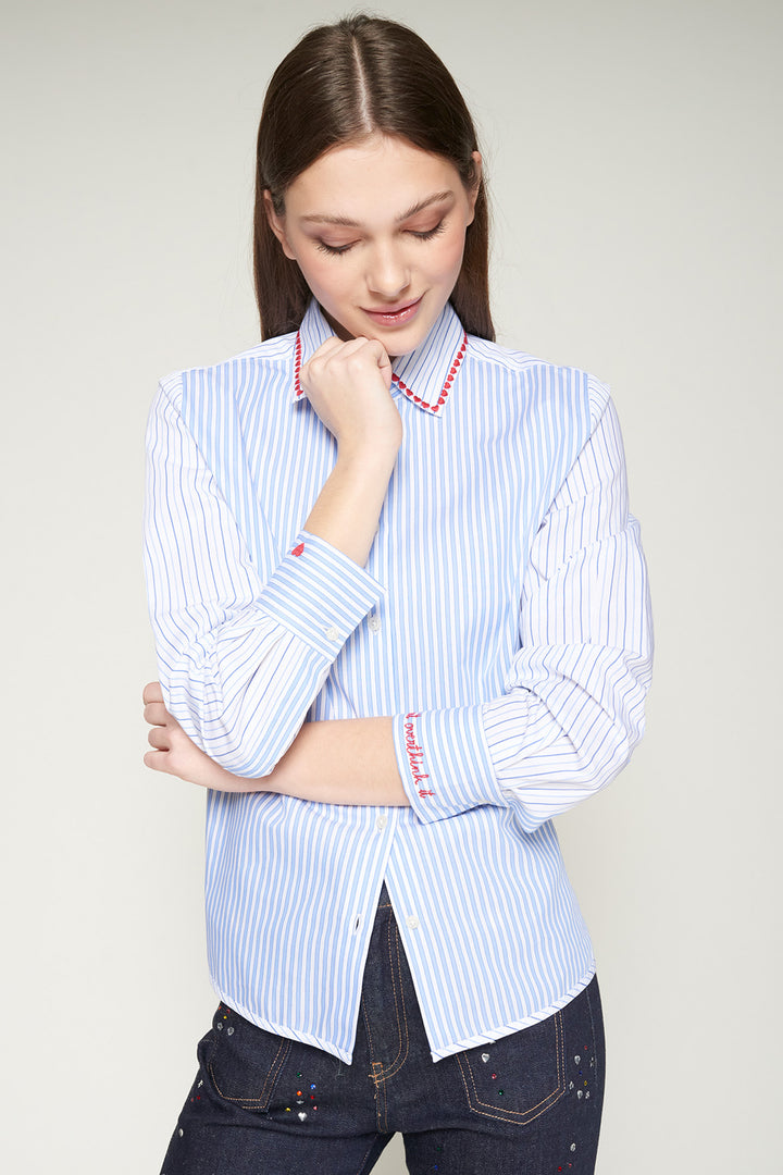 Woman wearing a light blue striped shirt with red accents on a plain background
