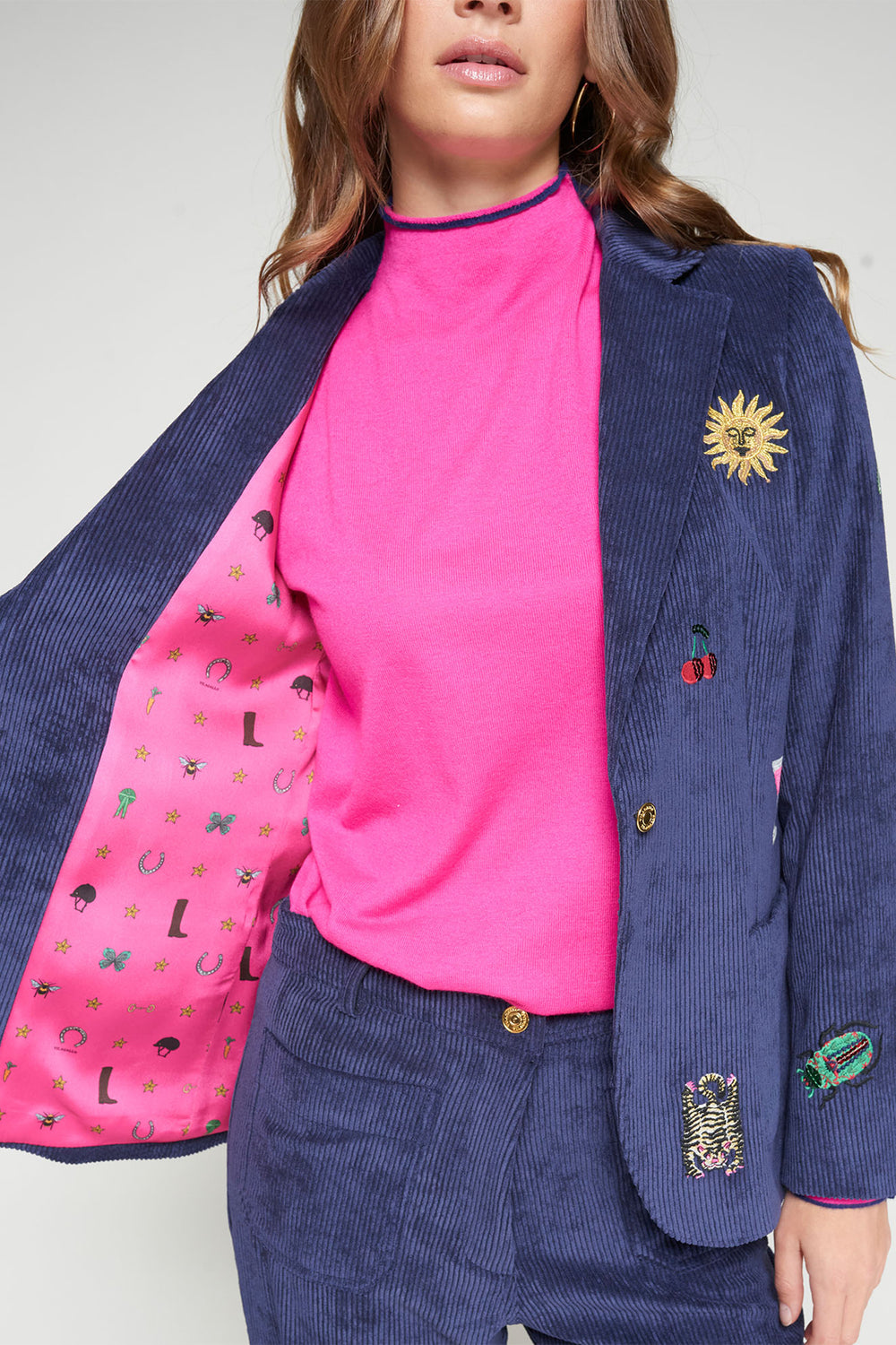 Person wearing a pink top and blue blazer with various pins on a white background