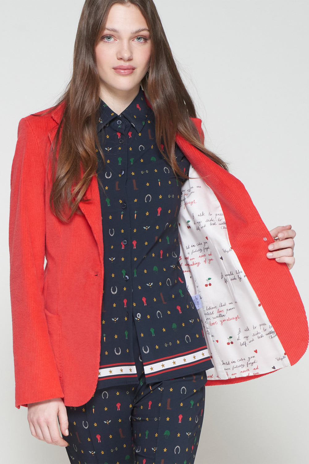 Woman wearing a red blazer over a patterned outfit with a white background
