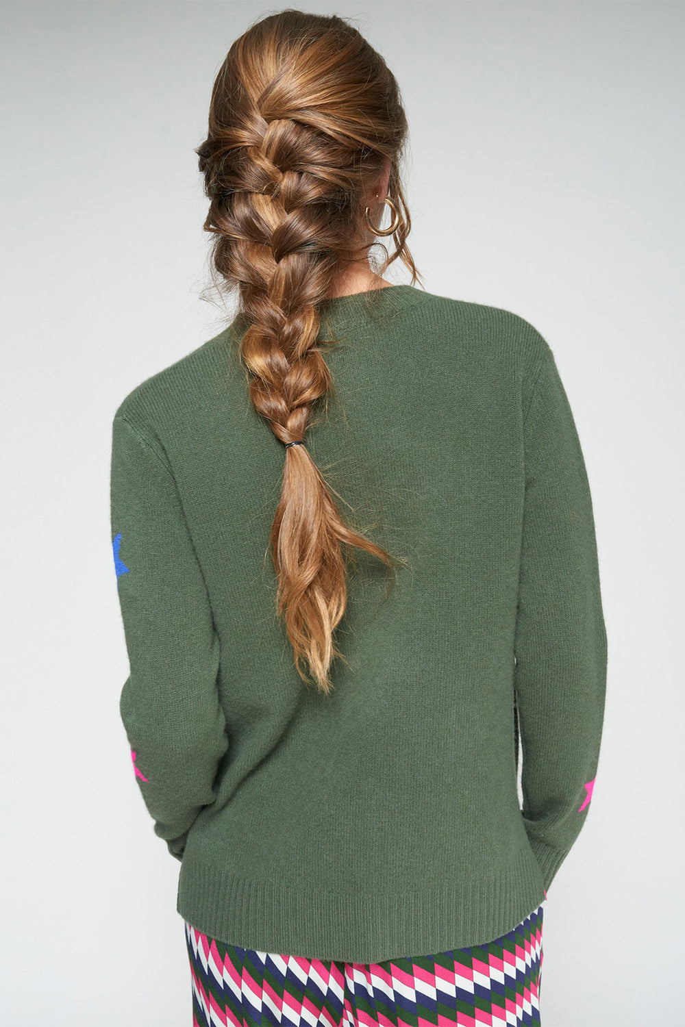 Person wearing a green cardigan with a braided hairstyle on a plain background