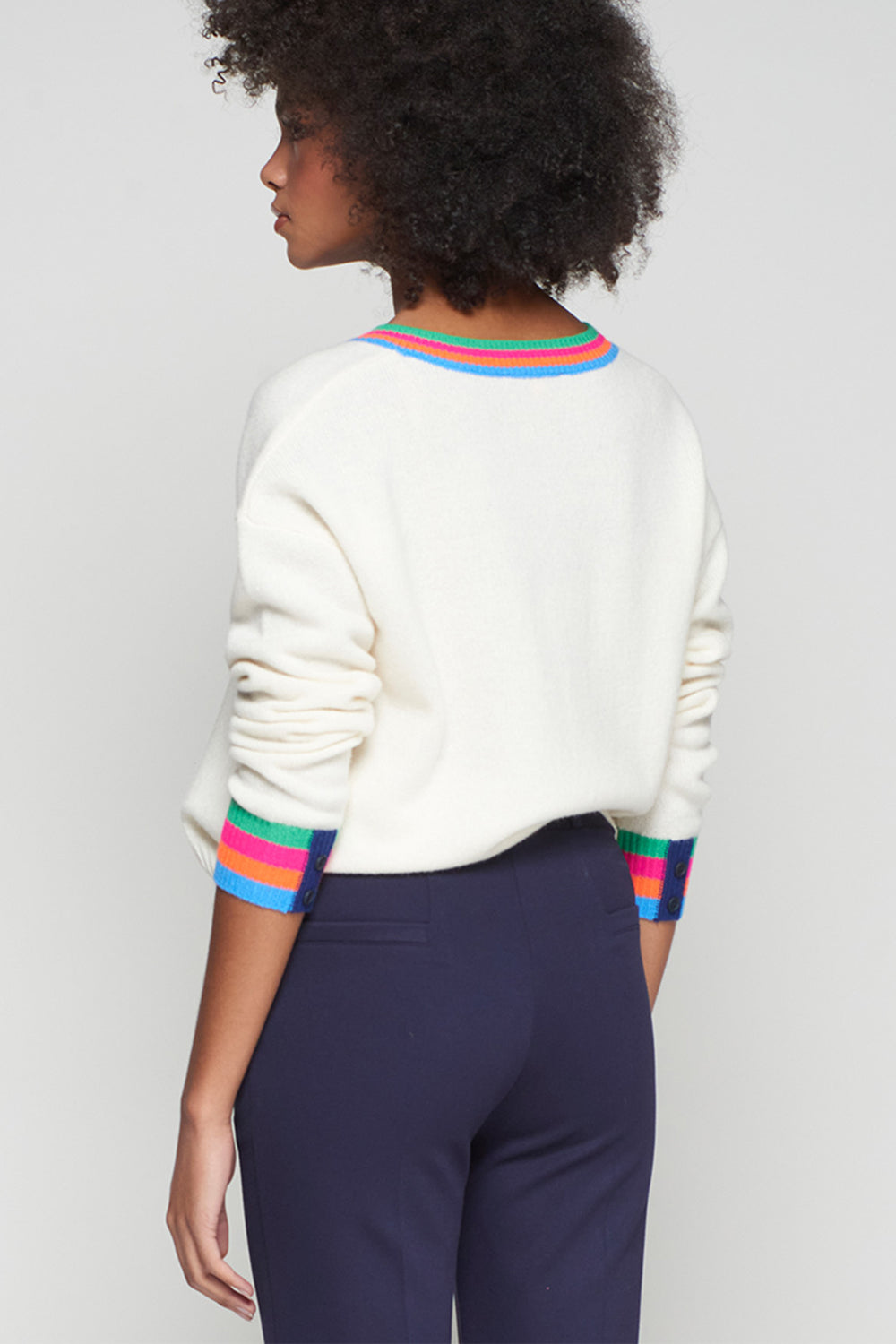 Person wearing a white sweater with colorful cuffs and hem against a plain background