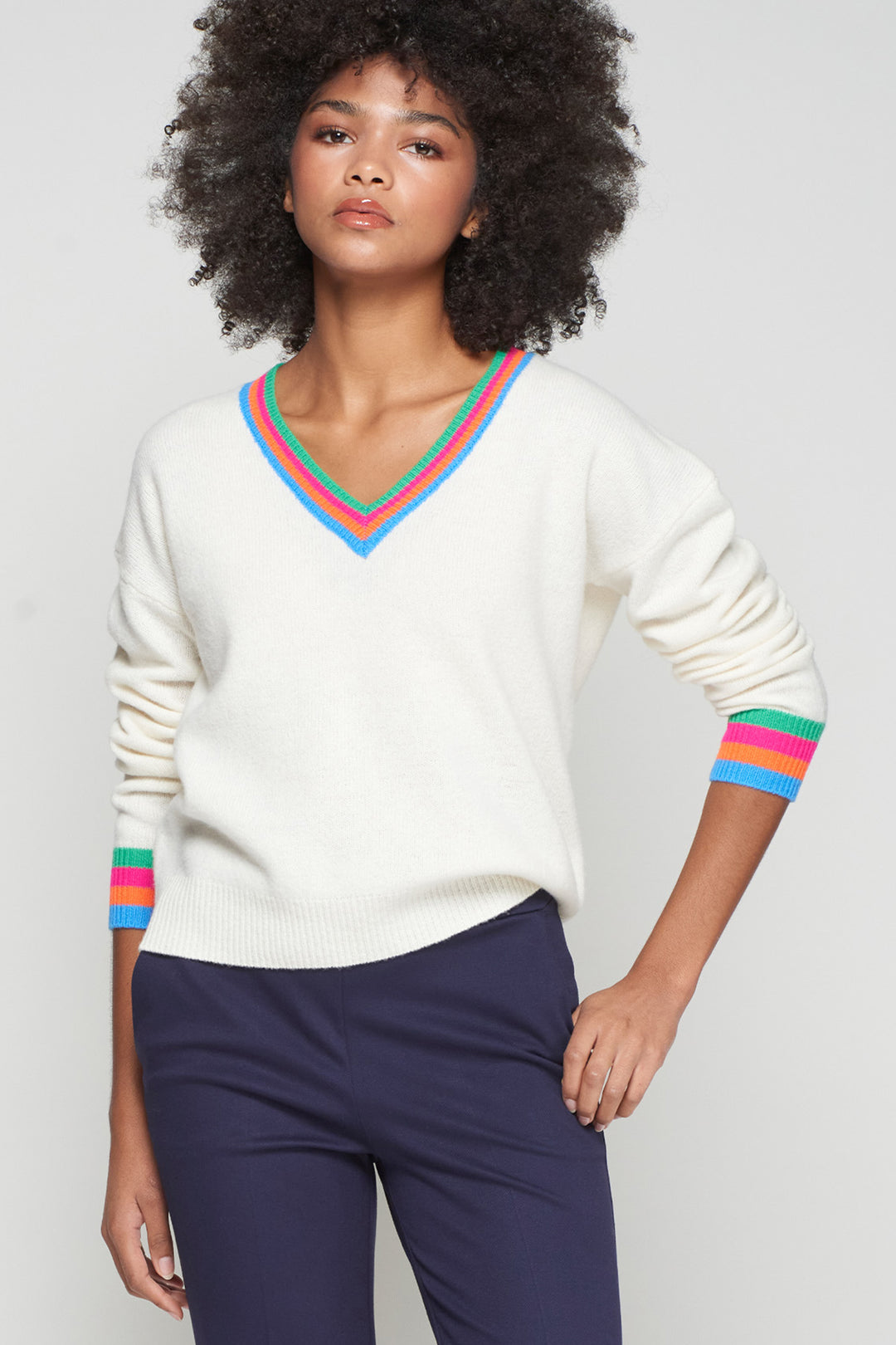 Woman wearing a white sweater with colorful stripes on a plain background