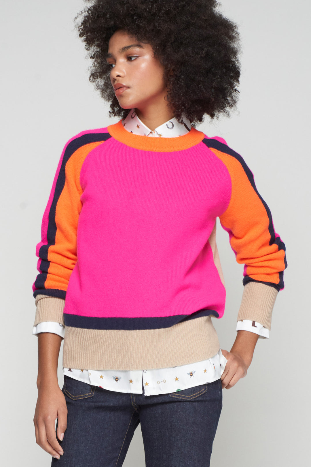 Person wearing a colorful sweater with pink, orange, and navy sleeves on a plain background