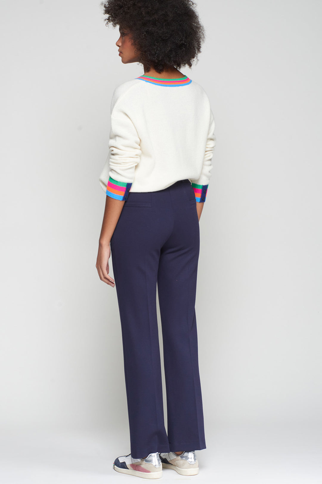 Person wearing a white sweater with colorful trim and navy pants on a plain background