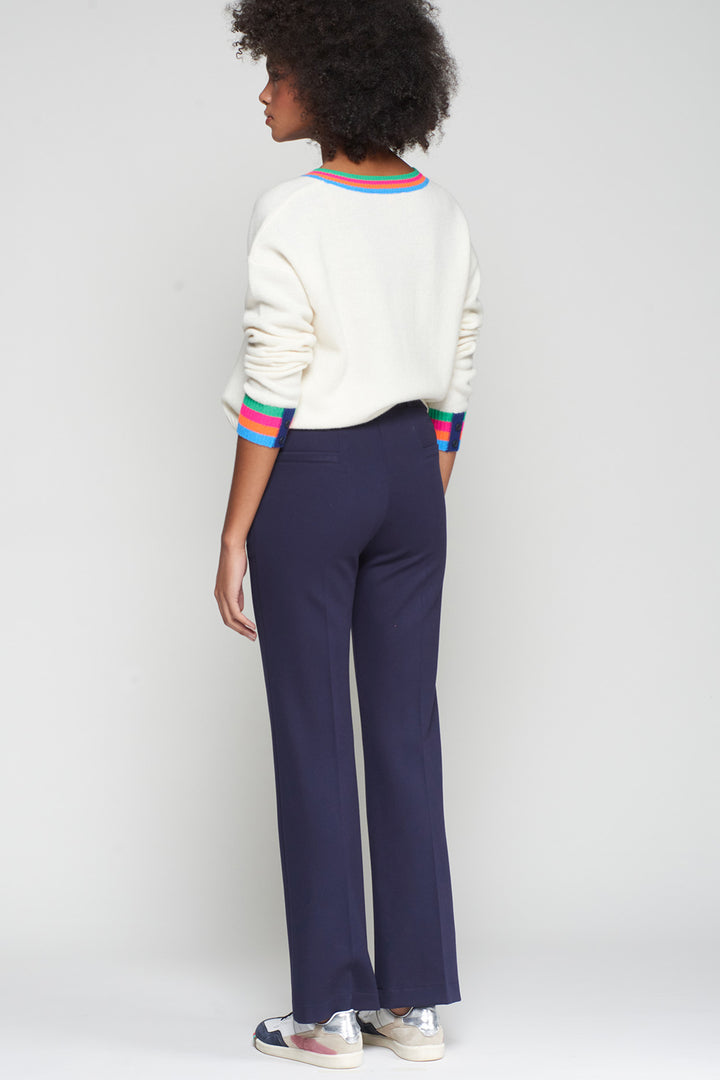 Person wearing a white sweater with colorful trim and navy pants on a plain background