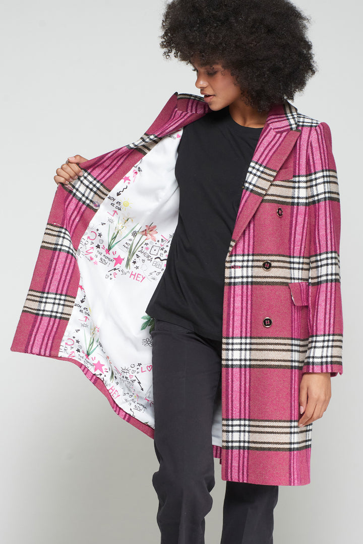 Person wearing a pink plaid coat with a floral lining, standing against a plain background