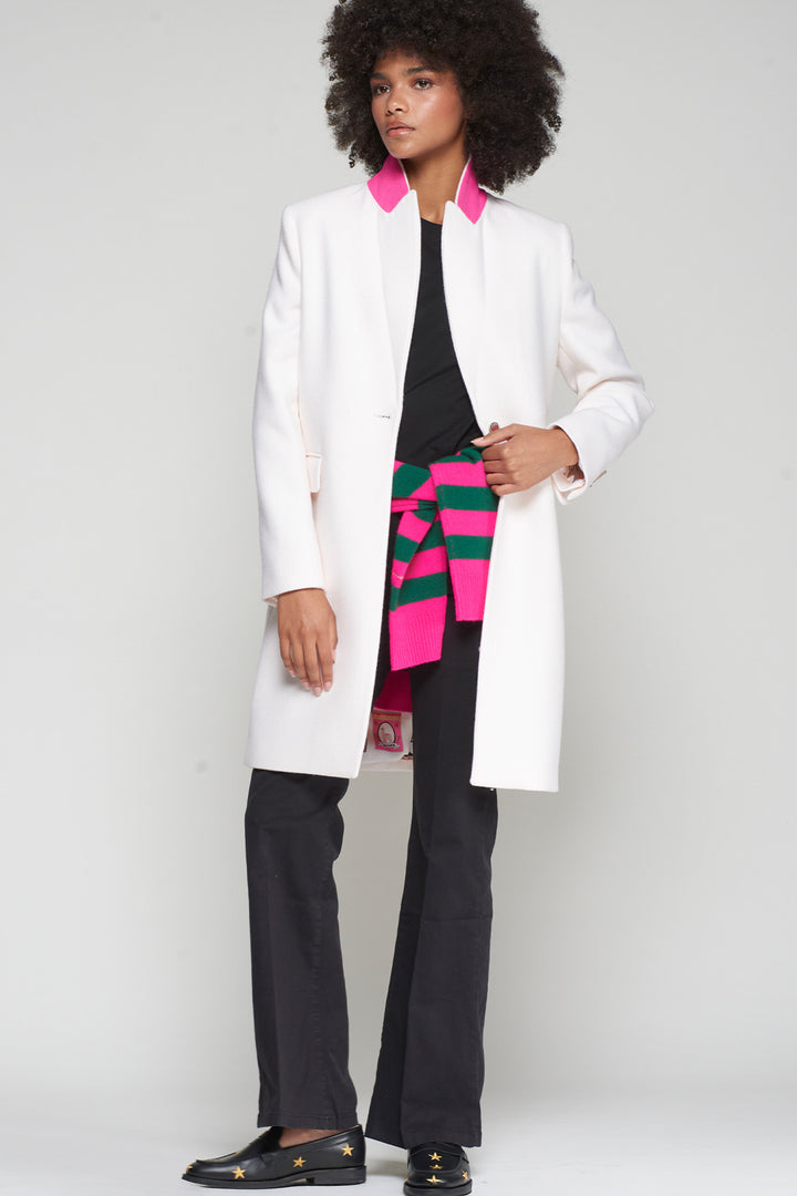 Person wearing a white coat over a colorful sweater with black pants on a plain background