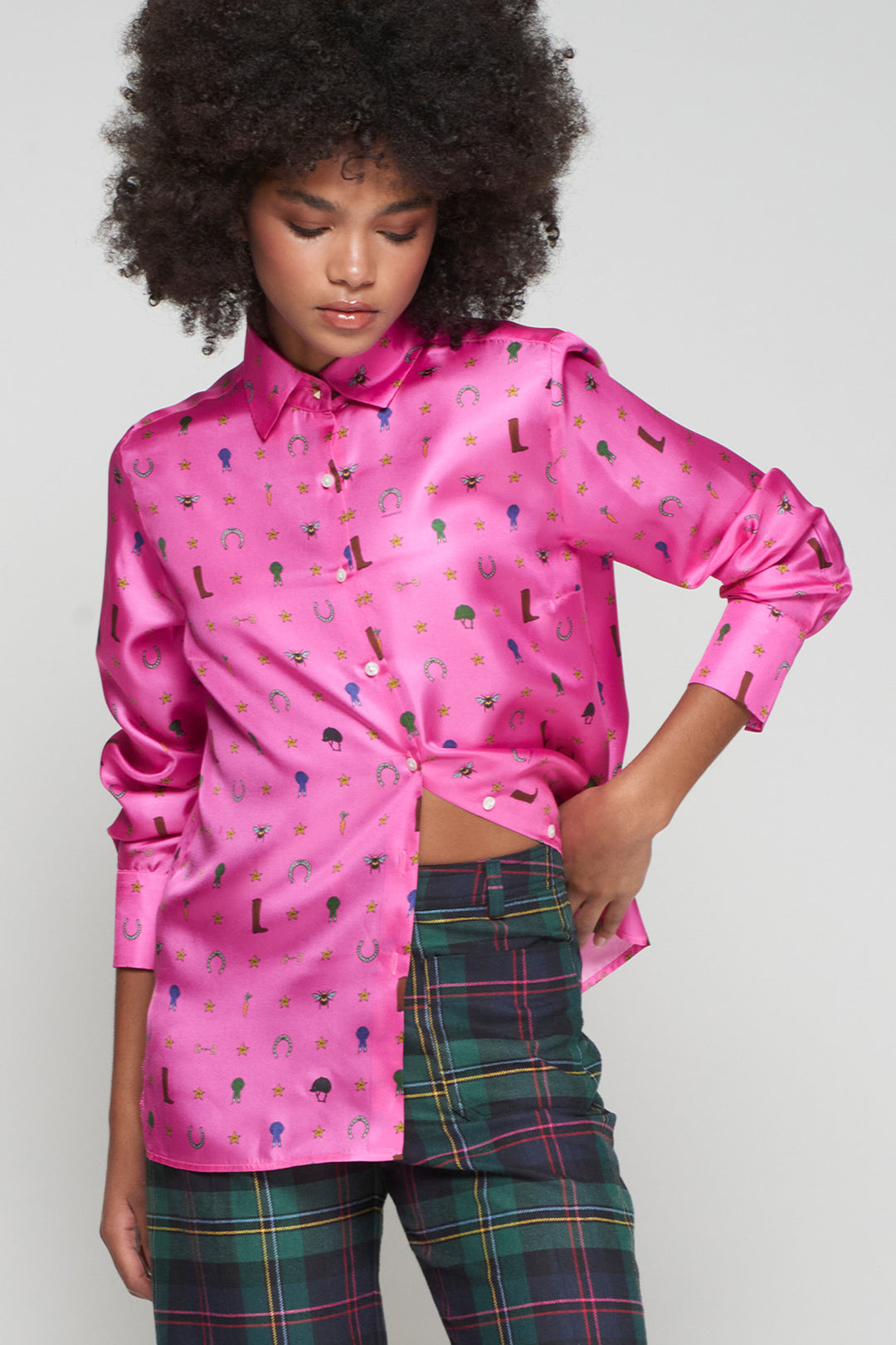 Person wearing a pink satin shirt with colorful patterns and plaid pants on a plain background