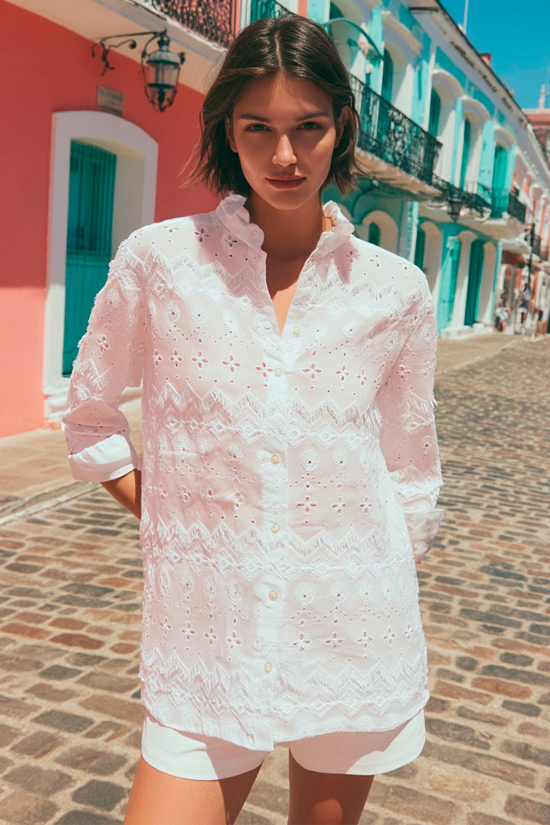 Woman wearing a white lace dress standing on a colorful street.