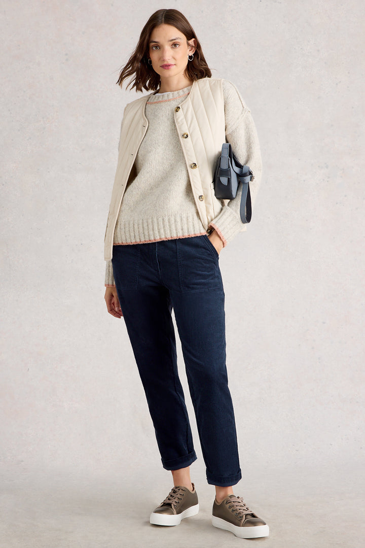Woman wearing a beige cardigan, white sweater, navy pants, and brown shoes on a light gray background