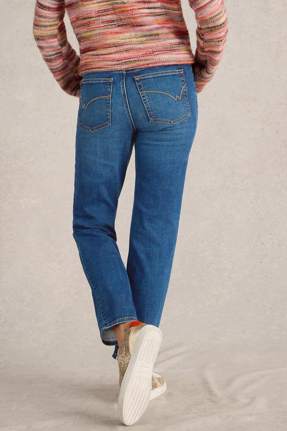 Person wearing blue jeans and a multicolored sweater on a beige background