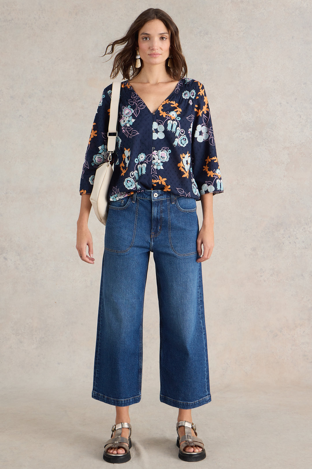 Woman wearing a floral top and blue jeans against a neutral background