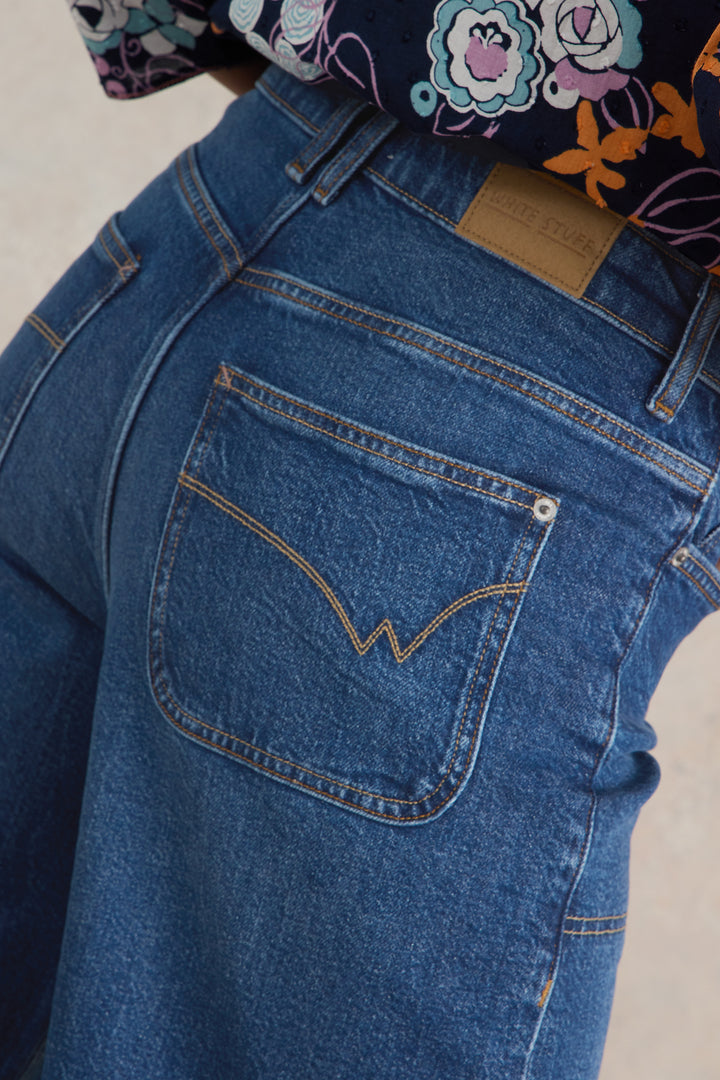 Close-up of blue jeans with a brand logo on the pocket against a neutral background